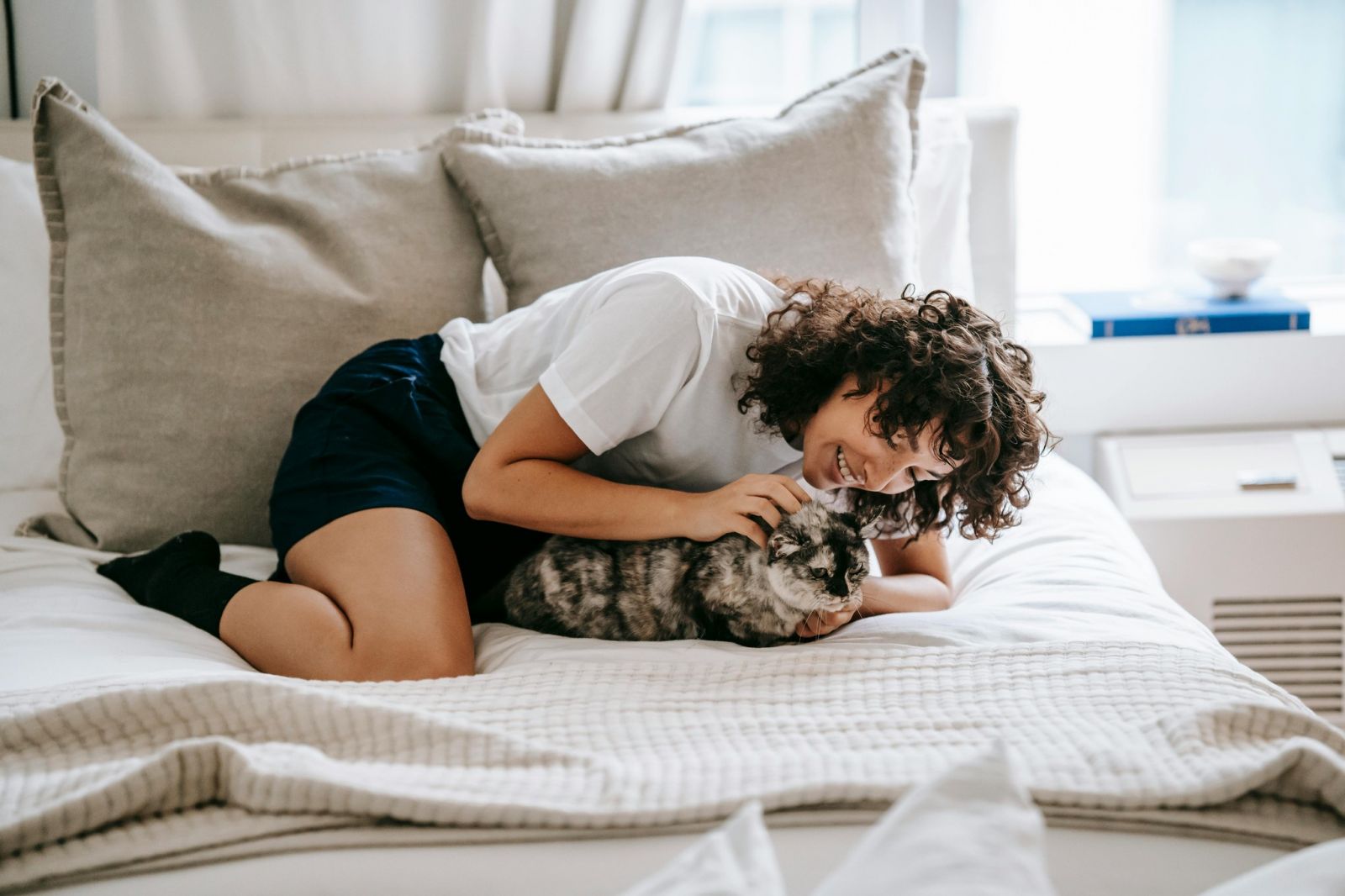 Young woman snuggling her cat on a bed near a window